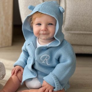 Baby Sitting In A Blue Hooded Knitted Baby Cardigan with Initial embroidered on front.