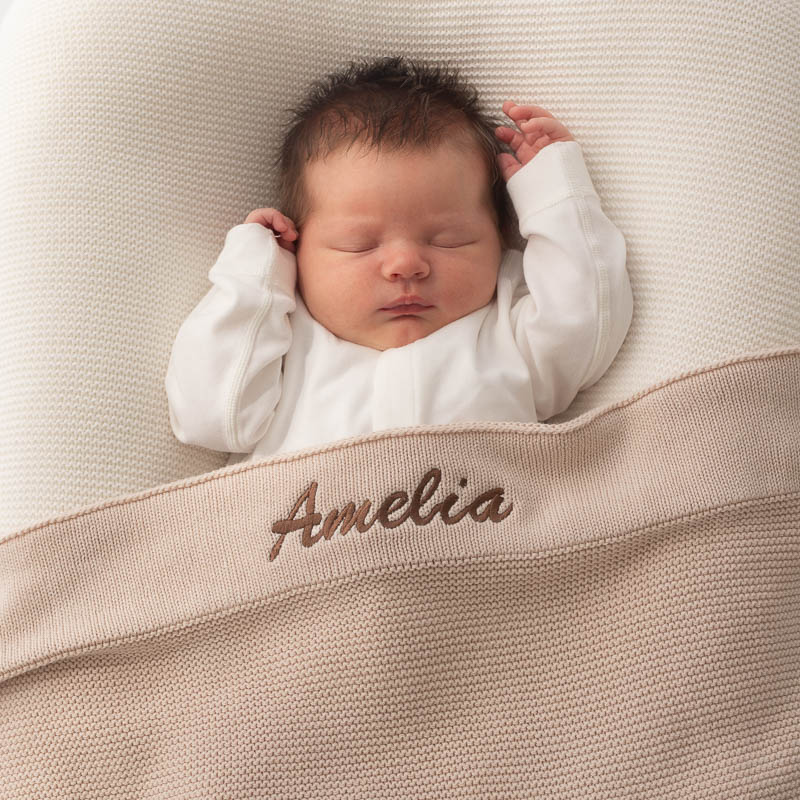 Baby sleeping under personalised beige knitted blanket.