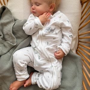 Sleeping baby in personalised white koala print zip romper in a rattan chair with sage blanket.