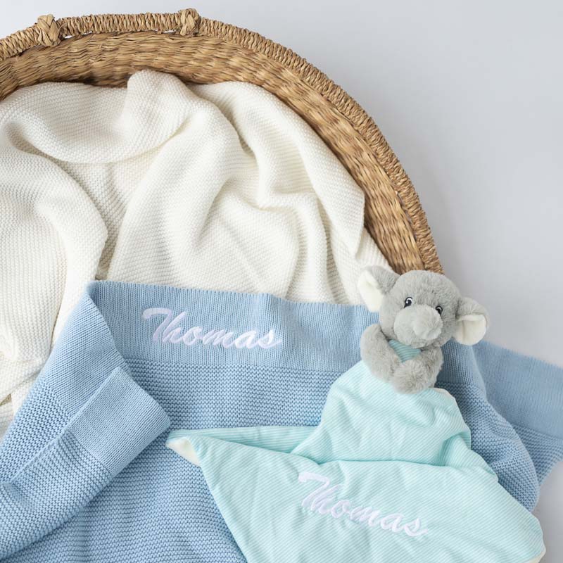 Personalised blue baby boy blanket and elephant comforter gift items in a basket.