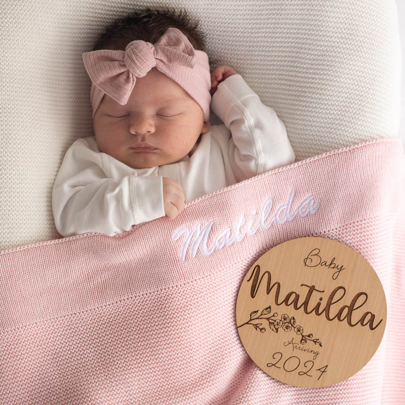 Baby with personalised pink knitted blanket and birth announcement disc gifts for newborn girls.
