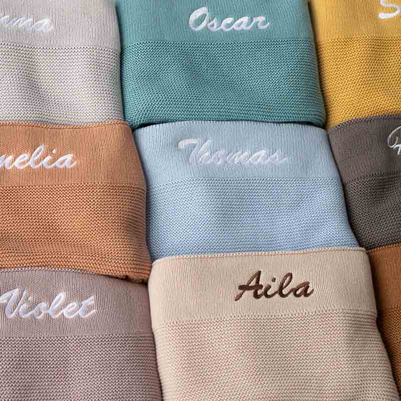 Personalised Knitted Baby Blankets Laid Out With Embroidery Showing.