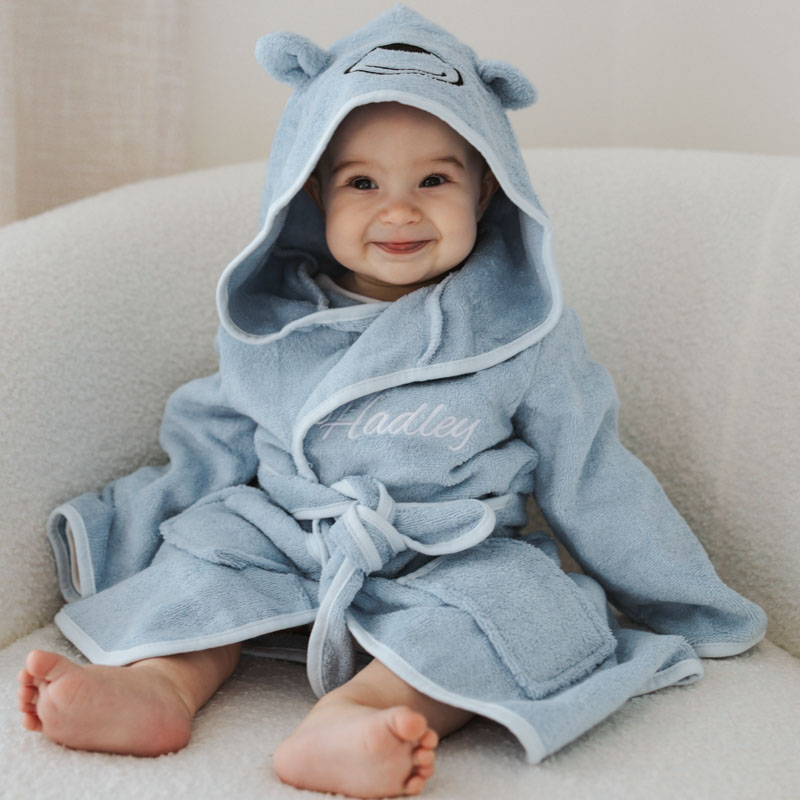 Smiling baby wearing a light blue hooded bathrobe with bear ears & embroidered name
