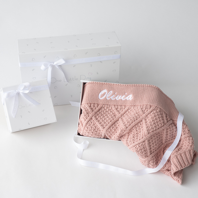 A blush pink diamond-knitted baby blanket with the name 