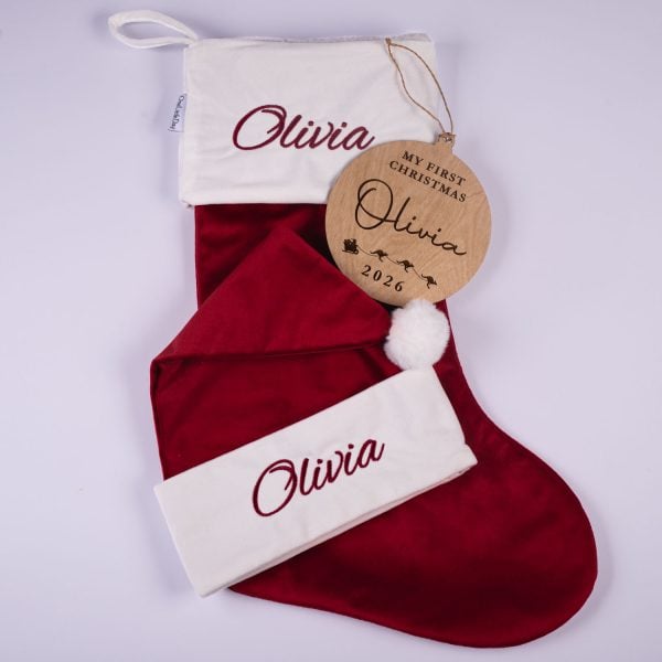 Burgundy Christmas Baby Hat, Stocking & Disc Olivia Burgundy velvet personalised baby Christmas stocking, matching Santa hat with white cuffs and wooden My First Christmas disc with engraved name and year on white background.