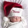 Burgundy Christmas Hat & Baby Sleeping baby wearing a personalised red and white Christmas hat embroidered with the name “Olivia.”