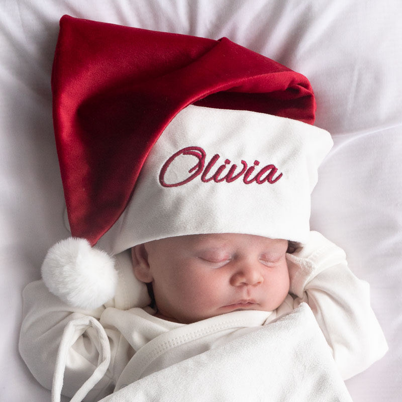 Sleeping baby wearing a personalised red and white Christmas hat embroidered with the name “Olivia.”