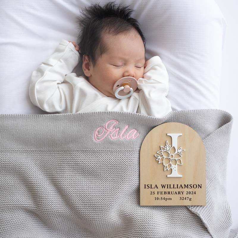 Newborn baby Isla sleeps peacefully with a pacifier, wrapped in a personalised grey knitted blanket.