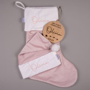 Light pink velvet personalised baby Christmas stocking and matching Santa hat with white cuffs and pink embroidered script name displayed alongside a wooden My First Christmas disc with engraved name and year.