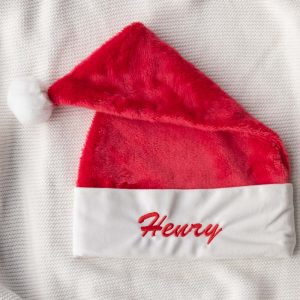 Red Christmas hat with white trim, embroidered with the name “Henry” in red script.
