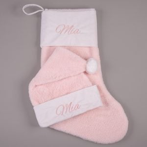 Pink faux fur personalised baby Christmas stocking and matching Santa hat with cream cuffs, pompom and pink embroidered script name on grey background.