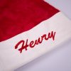 Red Christmas Baby Hat Close Up Close up of white velvet baby Santa hat cuff with red embroidered script name on red faux fur hat.