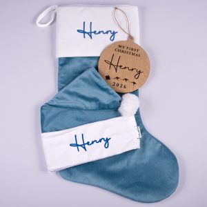 Sky blue velvet personalised baby Christmas stocking, matching Santa hat with white cuffs and wooden My First Christmas disc with engraved name and year on white background.