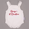 White 1st Christmas Newborn Romper George White knitted sleeveless newborn romper with shoulder straps, snap buttons and red embroidered personalised 1st Christmas text on grey background.