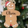 A Personalised Gingerbread Man Name Disc. Olivia Personalised wooden gingerbread man Christmas ornament with Olivia engraved and red Santa hat hanging on tree.