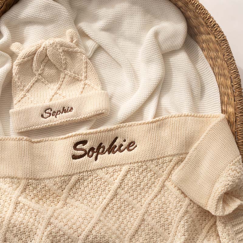 Cream knitted personalised baby blanket and beanie in bassinet.
