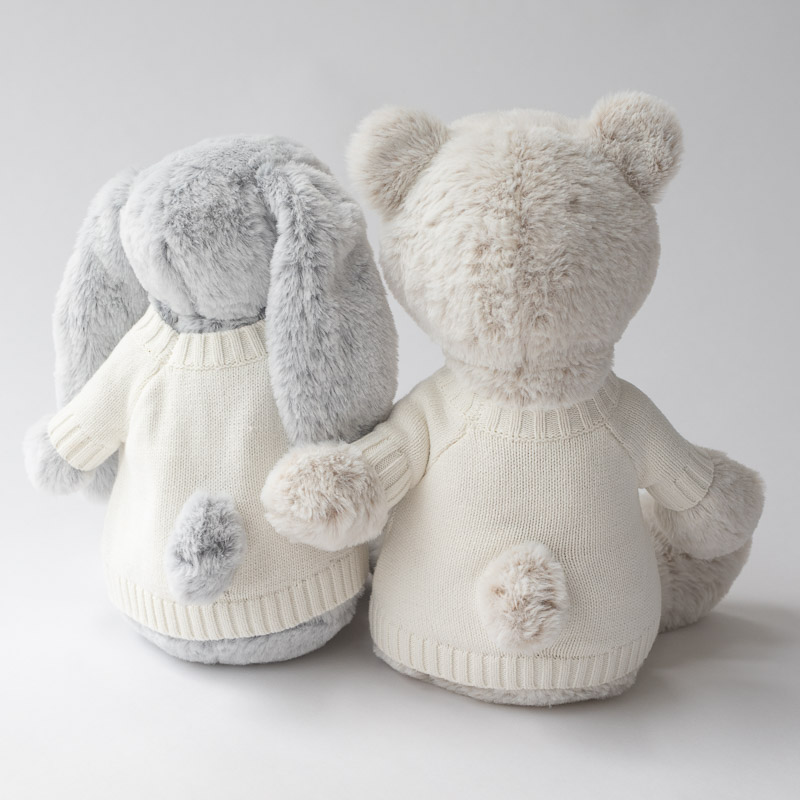 Plush bunny and bear in cream knit sweaters, sitting side by side with visible tails.
