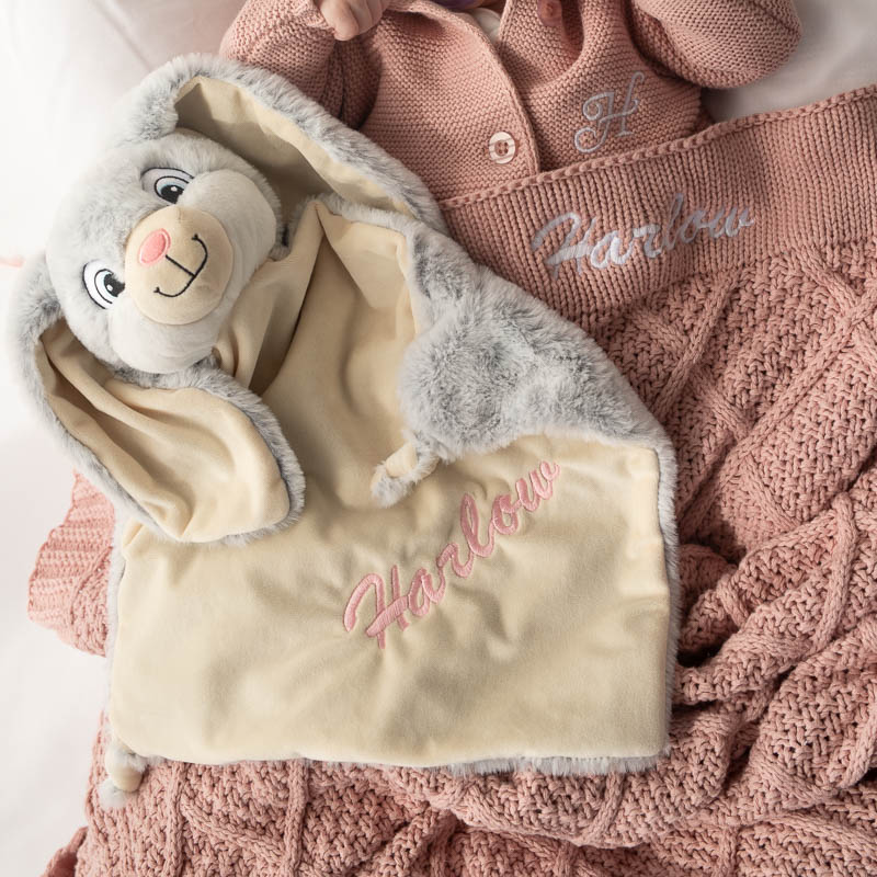 Baby with grey bunny comforter and blush pink diamong knitted blanket.