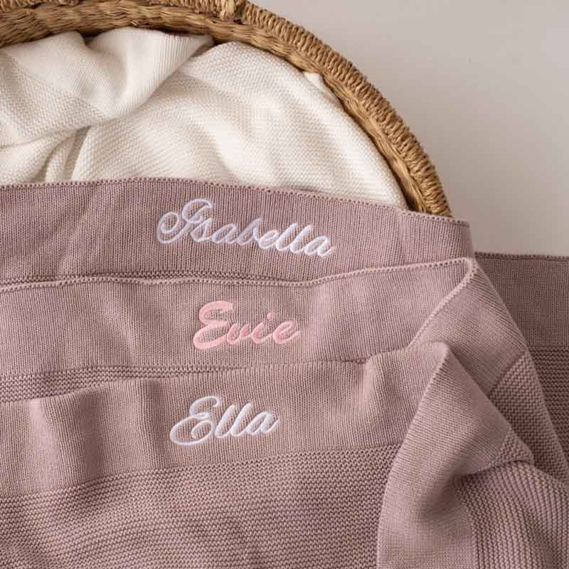 Three blush pink knitted blankets with embroidered names: Isabella, Evie, and Ella.