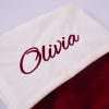 Close up of white velvet Christmas stocking cuff with burgundy embroidered script name on burgundy velvet stocking.