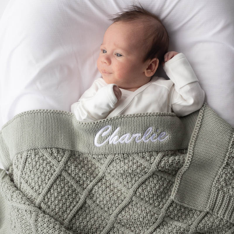 Baby wrapped in personalised green sage diamond knitted blanket embroidered with name Charlie.