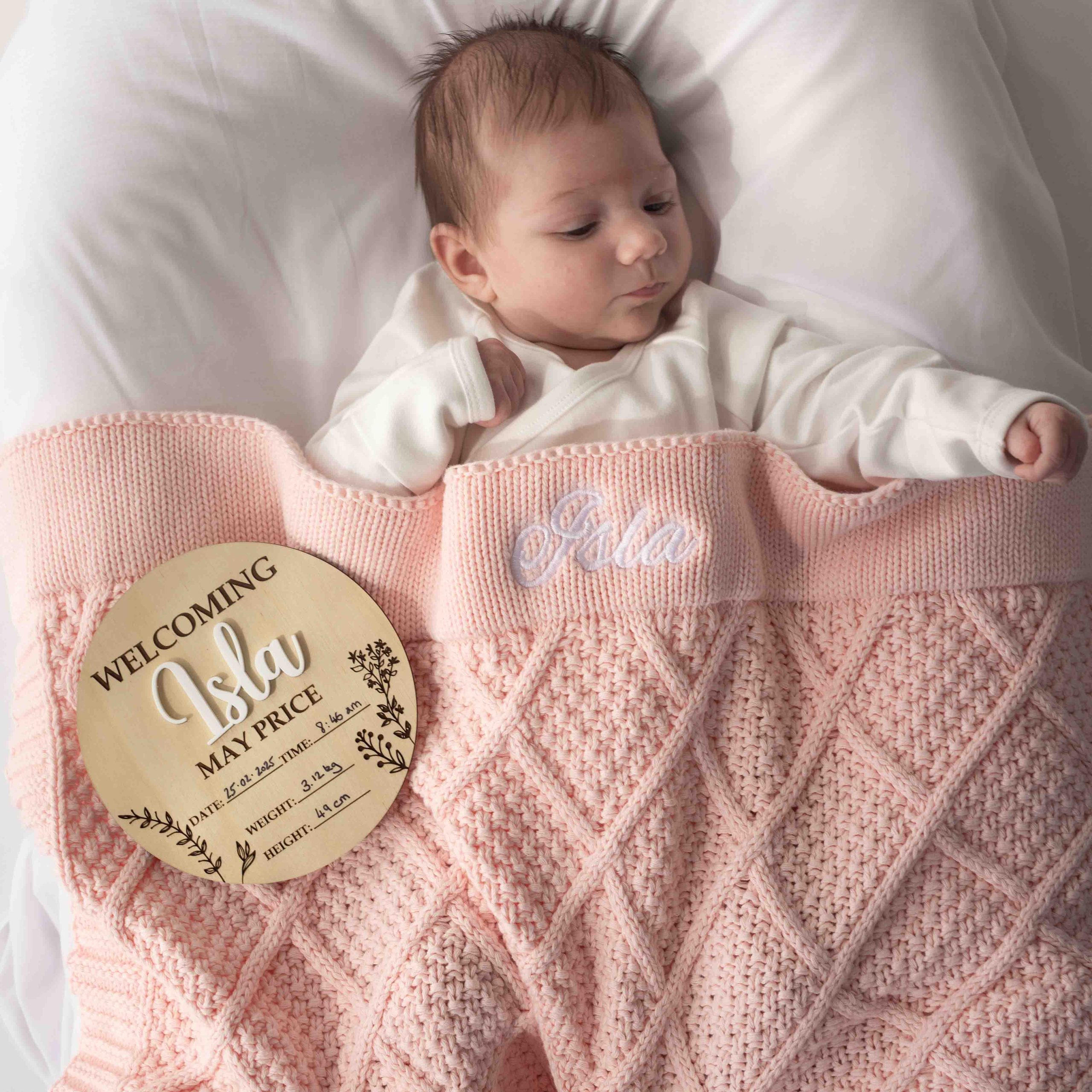 Baby wrapped in pink diamond knitted blanket with birth announcement disc.