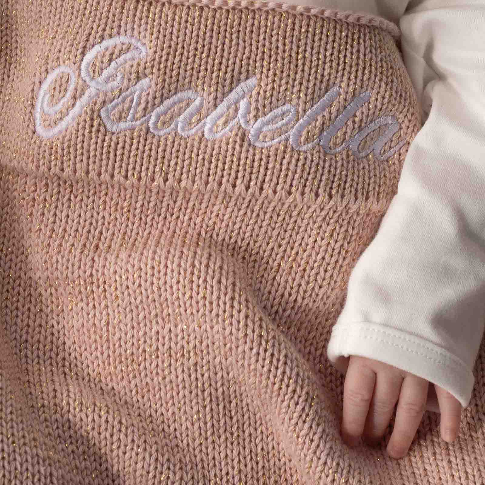 Baby wrapped in personalised pink & gold knitted blanket embroidered with the name Isabella.