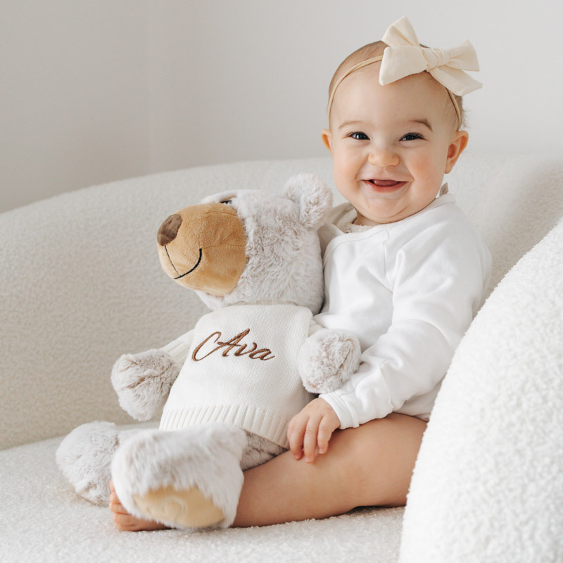 Baby smiling with personalised teddy bear named Ava.
