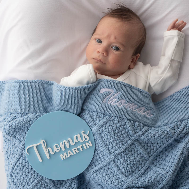 Baby wrapped in blue knitted blanket with blue name disc.