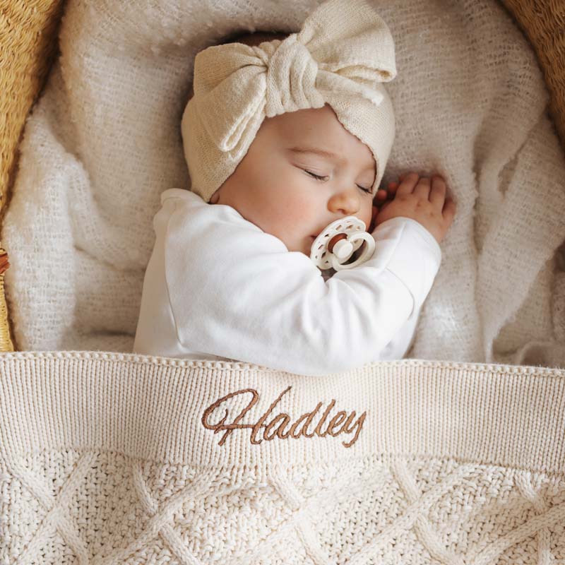 Baby sleeping with personalised cream knitted blanket and pacifier.