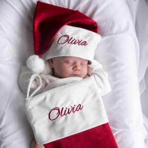 Baby wearing personalised burgundy Christmas hat and matching embroidered stocking from One Little Day.