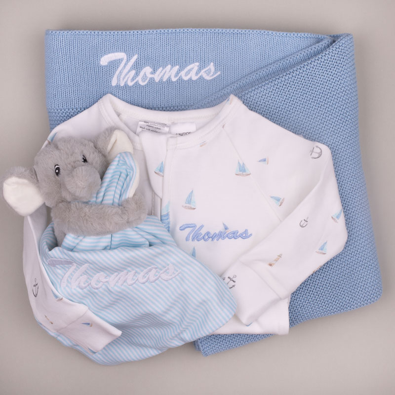 Blue Blanket Elephant Comforter Nautical Baby Onesie Nautical-print baby onesie, blue striped elephant comforter, and blue knitted blanket, all personalised with the name ‘Thomas.’