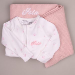 White baby onesie with pink butterflies and name ‘Isla,’ displayed on a pink knitted blanket with matching embroidery.