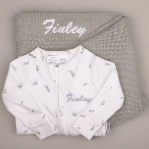 White koala-print baby onesie with name ‘Finley,’ displayed on a sage green knitted blanket with matching embroidery.