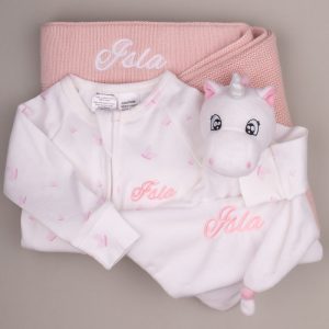 Soft pink-and-white baby gift set with personalized blanket, onesie, and unicorn comforter embroidered with the name “Isla.”