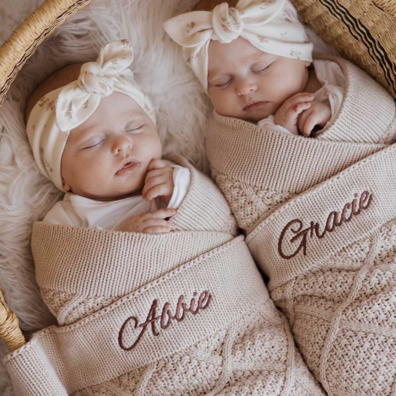 Two sleeping babies wrapped in beige personalised knitted blankets.