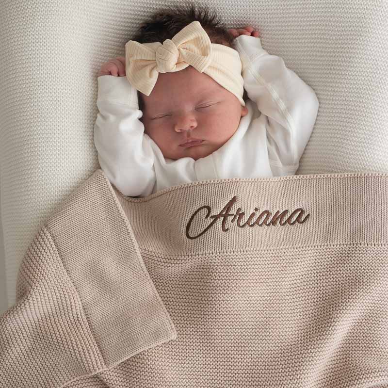 Sleeping newborn wrapped in personalised beige knitted baby blanket.