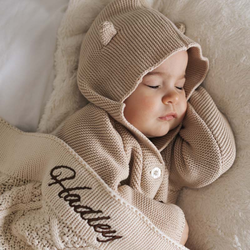 Beige knitted baby cardigan and personalised blanket.