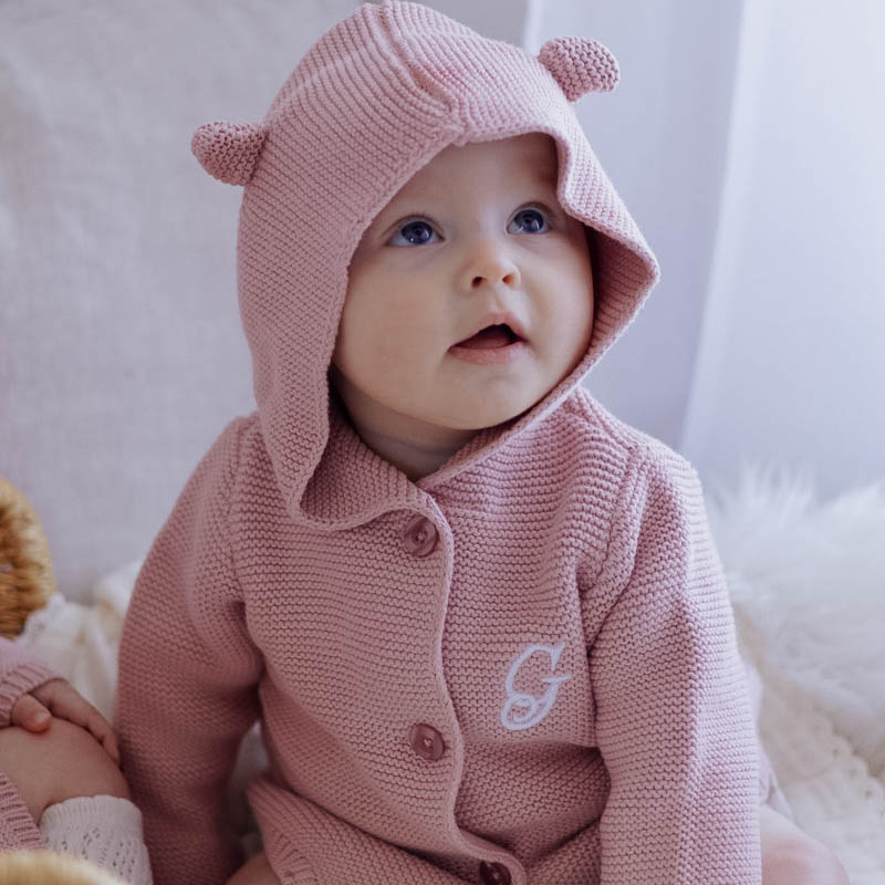 Baby wearing blush pink hooded knitted cardigan.