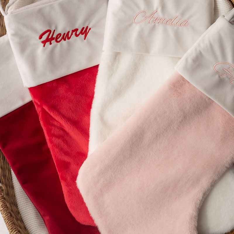 Four personalised Christmas stockings in pink, red, white and burgundy hanging together.