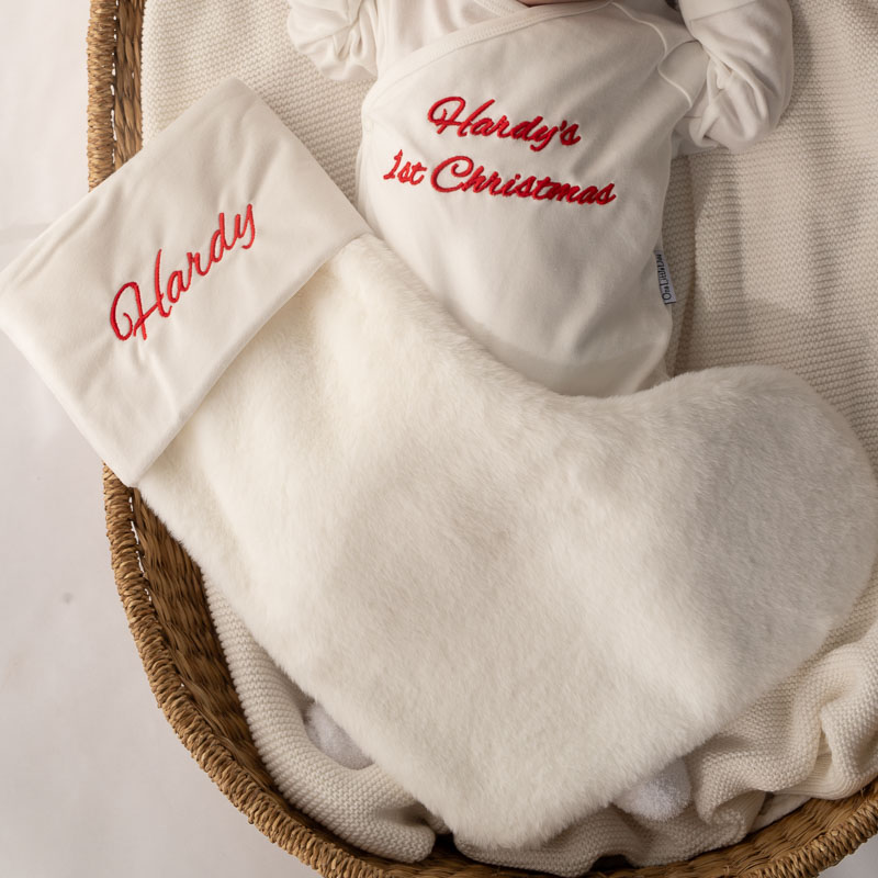 Baby wearing personalised first Christmas romper beside white Christmas stocking.