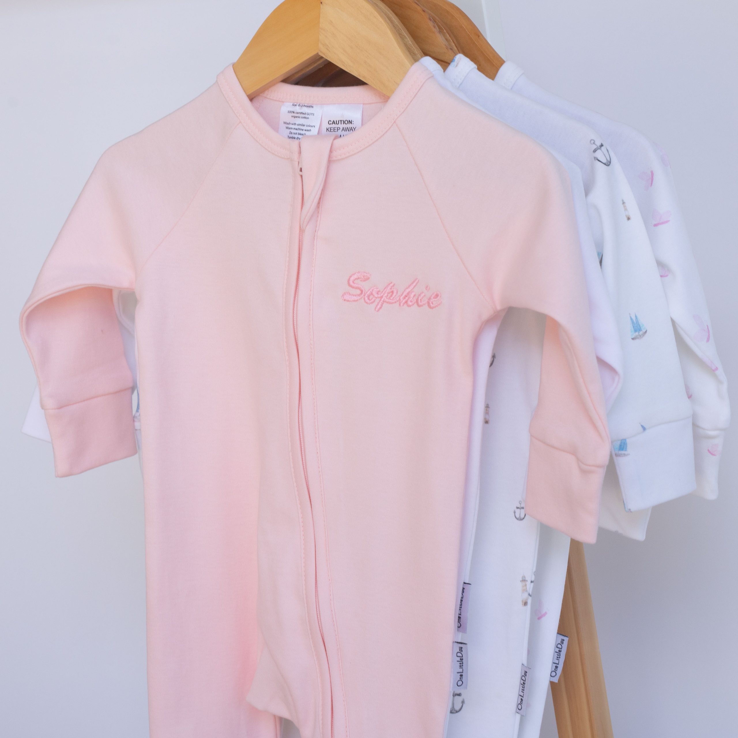 Pink personalised organic cotton baby zip onesie hanging on wooden hanger.