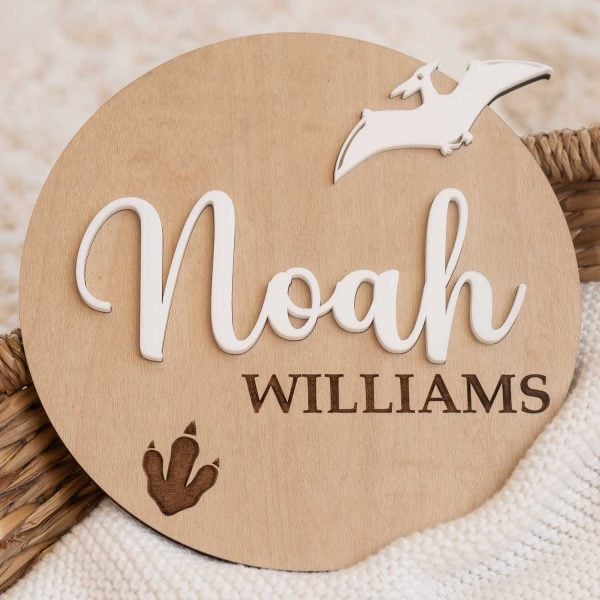 Baby Birth Announcement Dinosaur Disc Personalised wooden baby name disc with dinosaur design showing first and last name on knit blanket.
