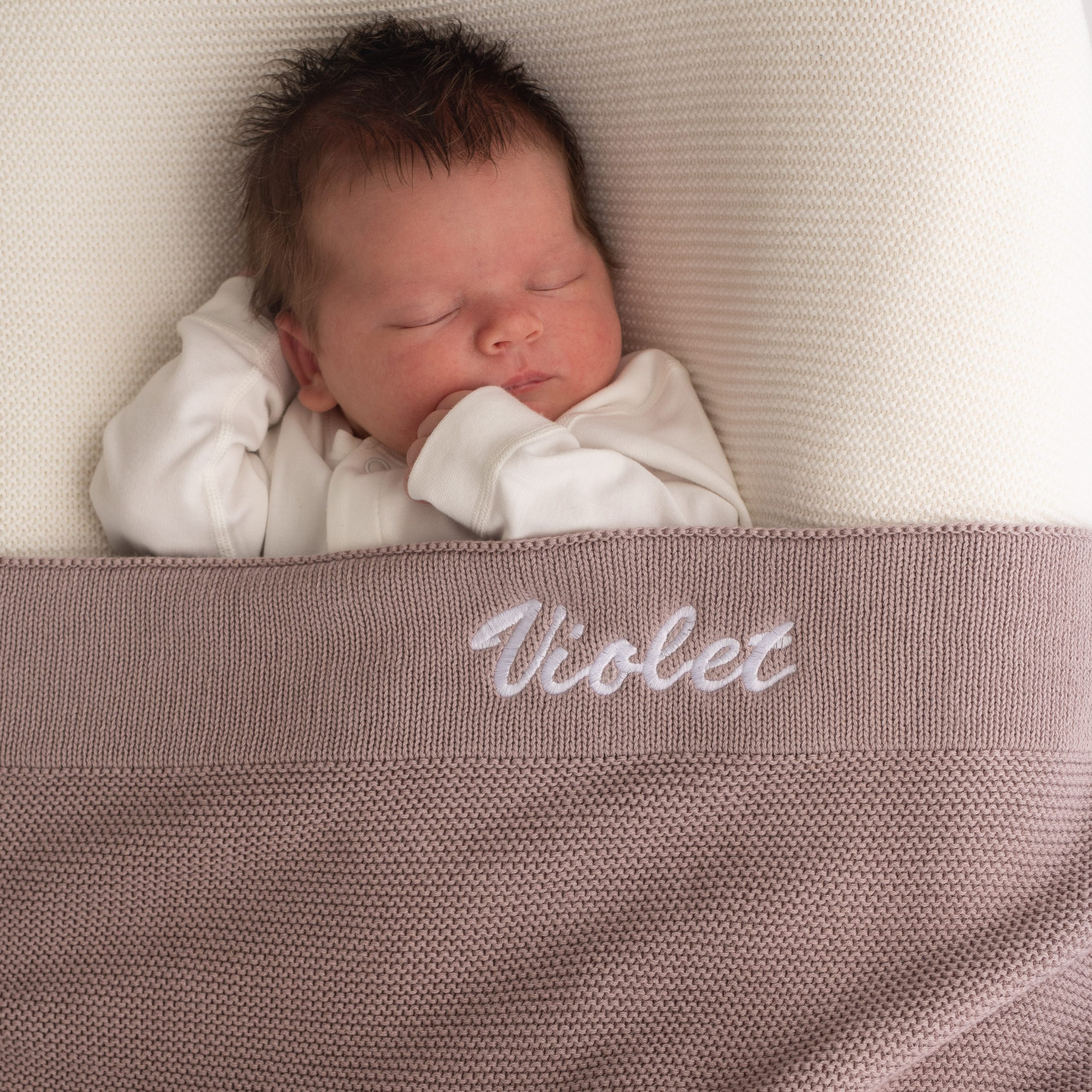 Sleeping newborn wrapped in dusty lilac personalised knitted baby blanket.