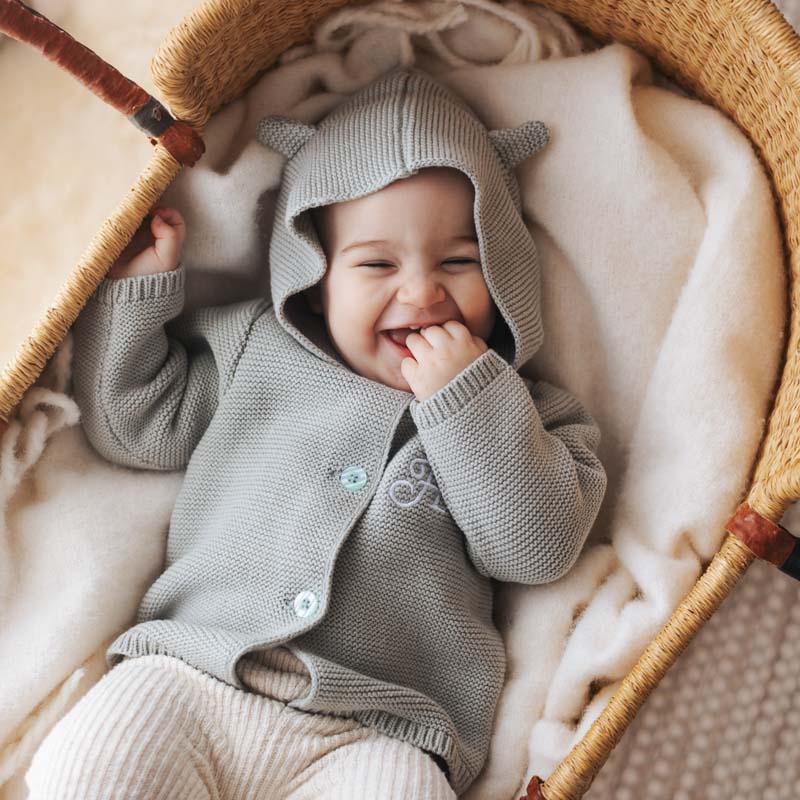 Smiling baby wearing sage green hooded knitted cardigan.