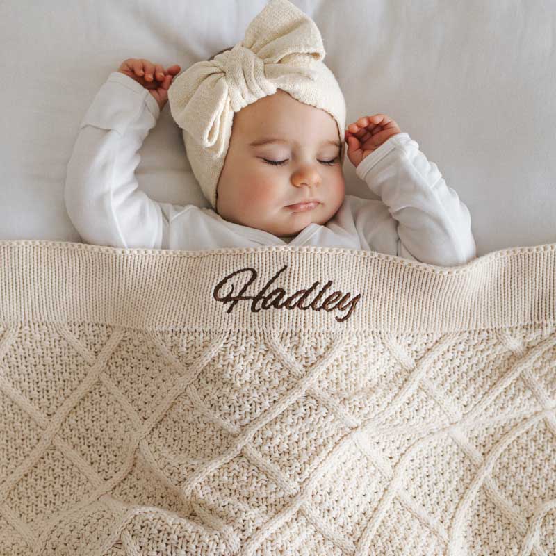 Newborn baby wrapped in personalised blue diamond knitted blanket.