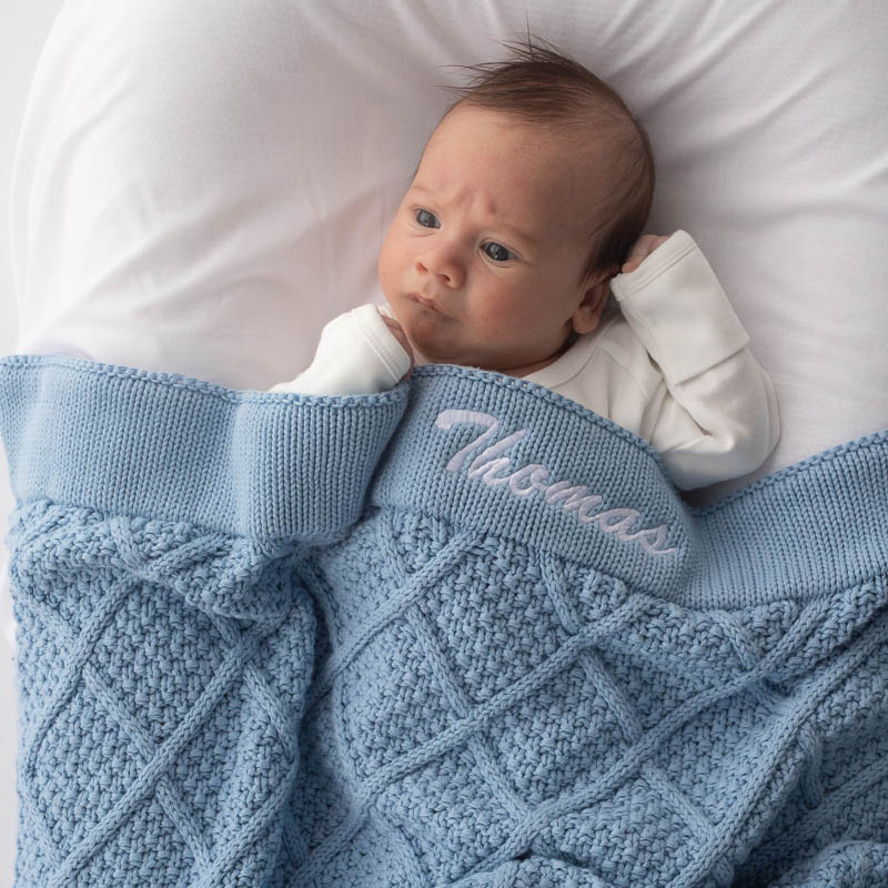 Baby resting under personalised blue diamond knitted blanket.