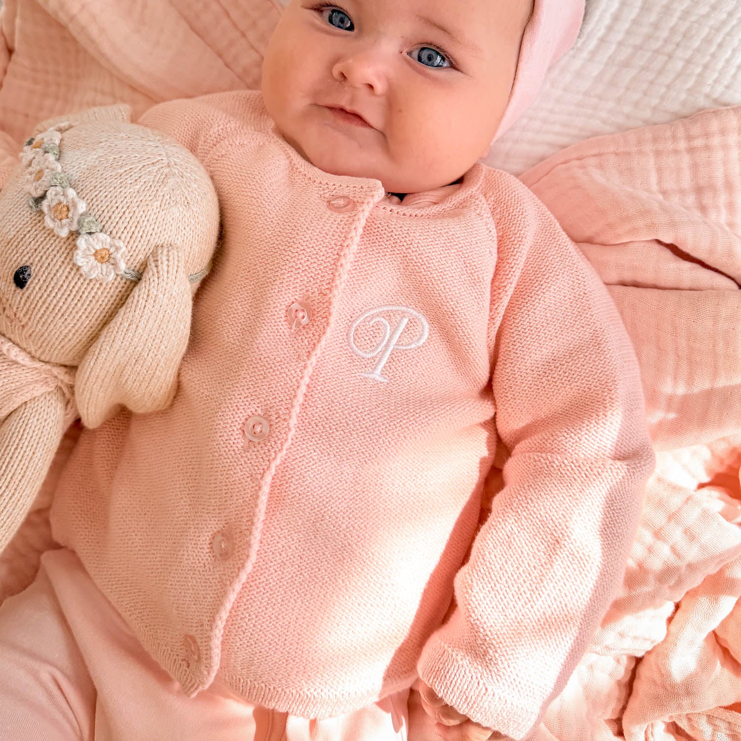Personalised pink knitted cardigan with monogram P embroidered in white on baby beside knitted bunny toy