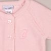 Close-up of pink knitted baby cardigan with buttons and embroidered letter “C” on chest.