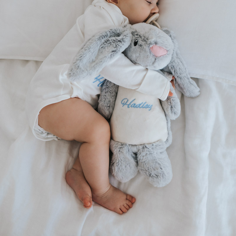 Baby sleeping while cuddling a personalised plush bunny.
